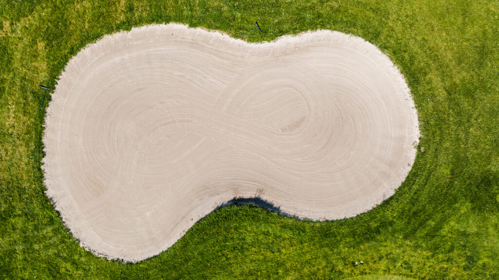 Bunker da golf visto dall’alto realizzato con sistema Capillary Bunkers, sabbia perfettamente drenata e bordo definito su tappeto erboso verde.